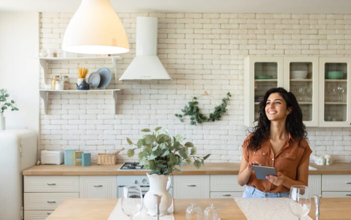 Beautiful young woman using digital tablet, browsing web or social media, working online, checking new app, having virtual conference with friend at kitchen, empty space