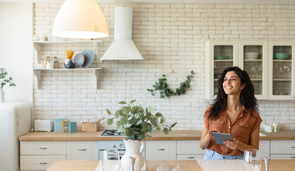 Beautiful young woman using digital tablet, browsing web or social media, working online, checking new app, having virtual conference with friend at kitchen, empty space